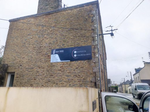 Bâtiment en pierre avec un panneau publicitaire sur la façade. Temps couvert.